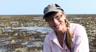 Sue Morrison crouched down on a reef talking to the camera